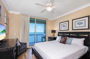 Habitación de hotel con cama, televisión, ventilador de techo, ventana con cortinas y cuadros en la pared.