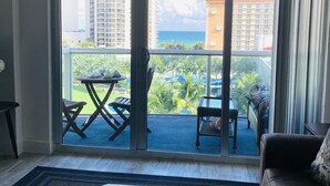 Ein geräumiges Wohnzimmer mit einem großen Schiebeglasfenster, das auf einen Balkon mit Sitzmöbeln und Blick auf das Meer und Gebäude führt.