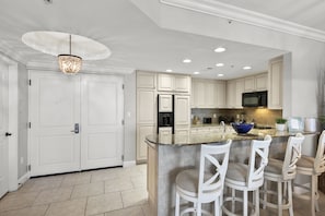 A modern kitchen with white cabinetry, a granite countertop, and a bar area with white stools.