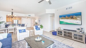 A modern living room with a flat-screen TV, a dining area with a chandelier, and a kitchen with wooden cabinets.