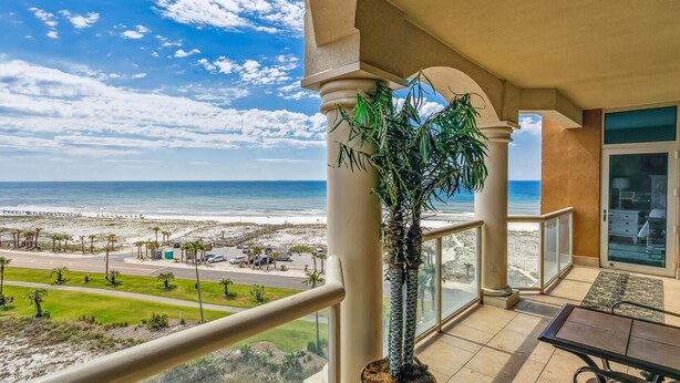 Un balcón con vista a la playa y al océano, una palmera y una puerta de vidrio.