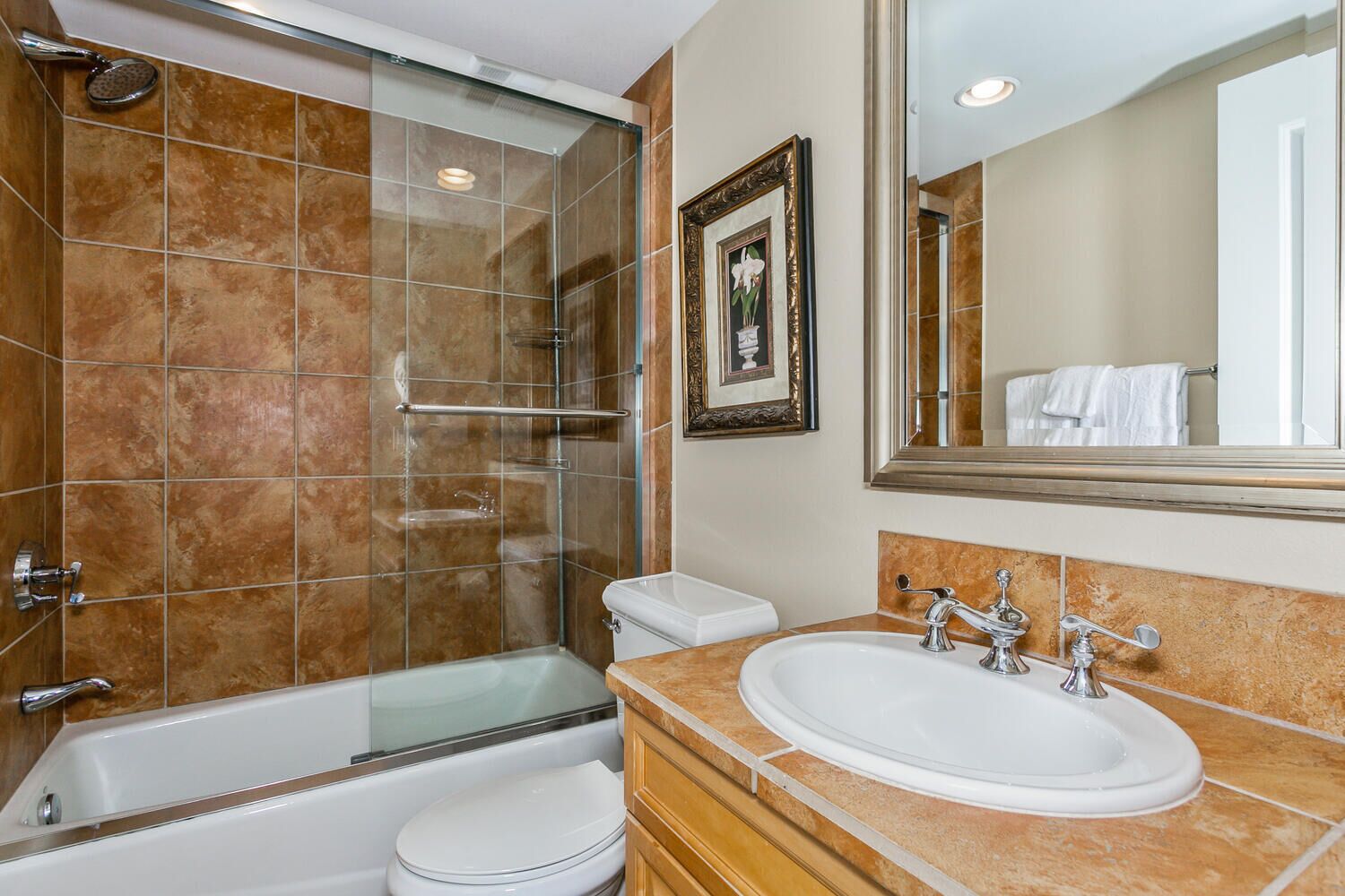 Un baño con ducha envuelta en cristal, inodoro blanco y lavabo con espejo superior.