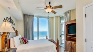 Habitación de hotel con cama, televisor, ventilador de techo y vista al océano.