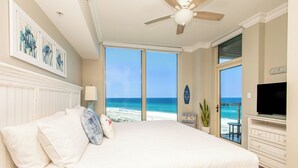 Une chambre avec un grand lit, un ventilateur de plafond, une télévision et une vue sur la plage.