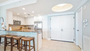 Une cuisine moderne avec des meubles blancs, un îlot central doté de tabourets, des appareils en acier inoxydable et des spots encastrés au plafond.