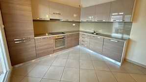 A modern kitchen with wooden cabinets, a stainless steel sink, and a tiled floor. - Apartment 85m2 luxury residence sea view 6 people 2 bedrooms (Porto-Vecchio)