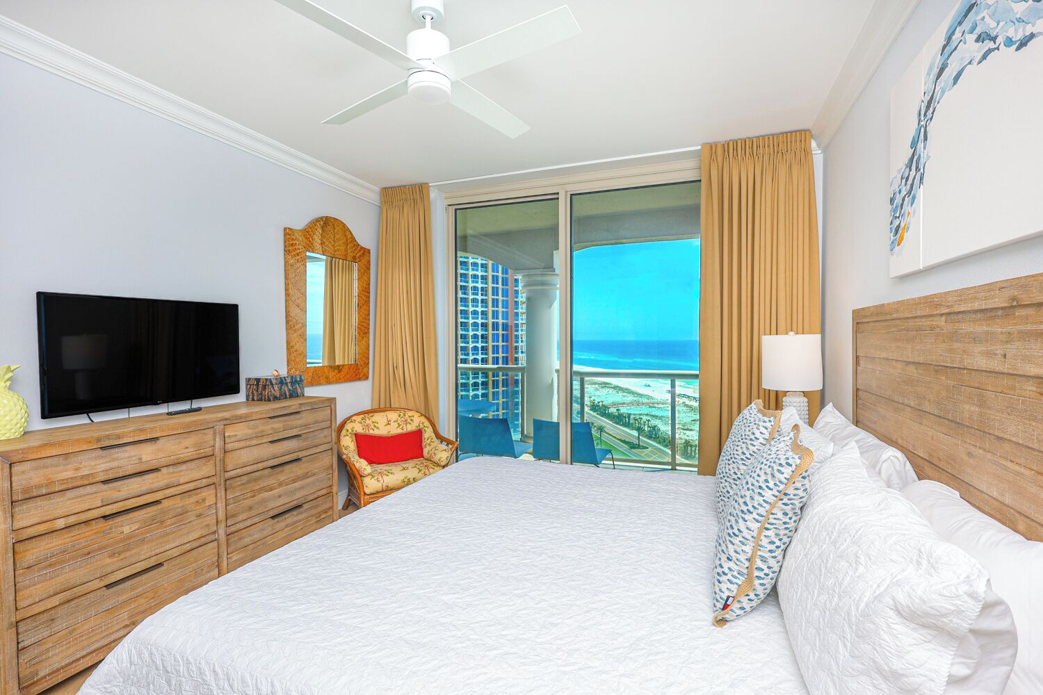 Habitación de hotel con una cama grande, televisión, muebles de madera, vista a la playa y un balcón.