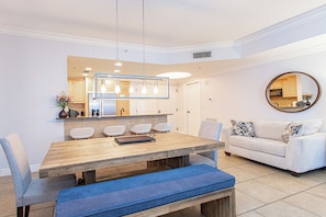 Een moderne keuken met witte kasten, een houten eettafel met blauwe kussens en een witte bank met gestreepte kussens.