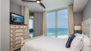 Een slaapkamer met een groot bed, een televisie op een dressoir en uitzicht op de oceaan.