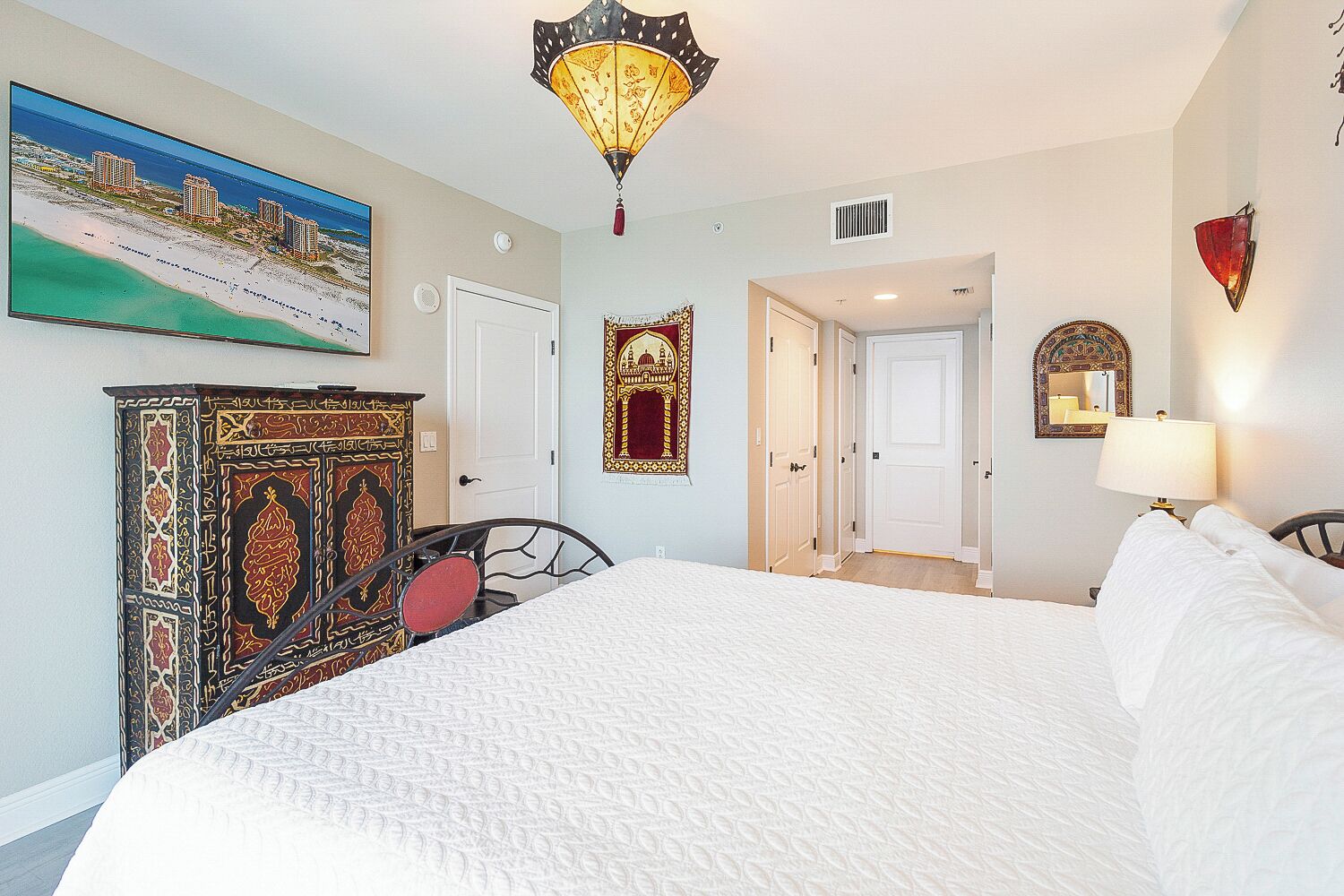 Une chambre d’hôtel avec un grand lit, une commode décorative, un tableau représentant une plage et un lustre.