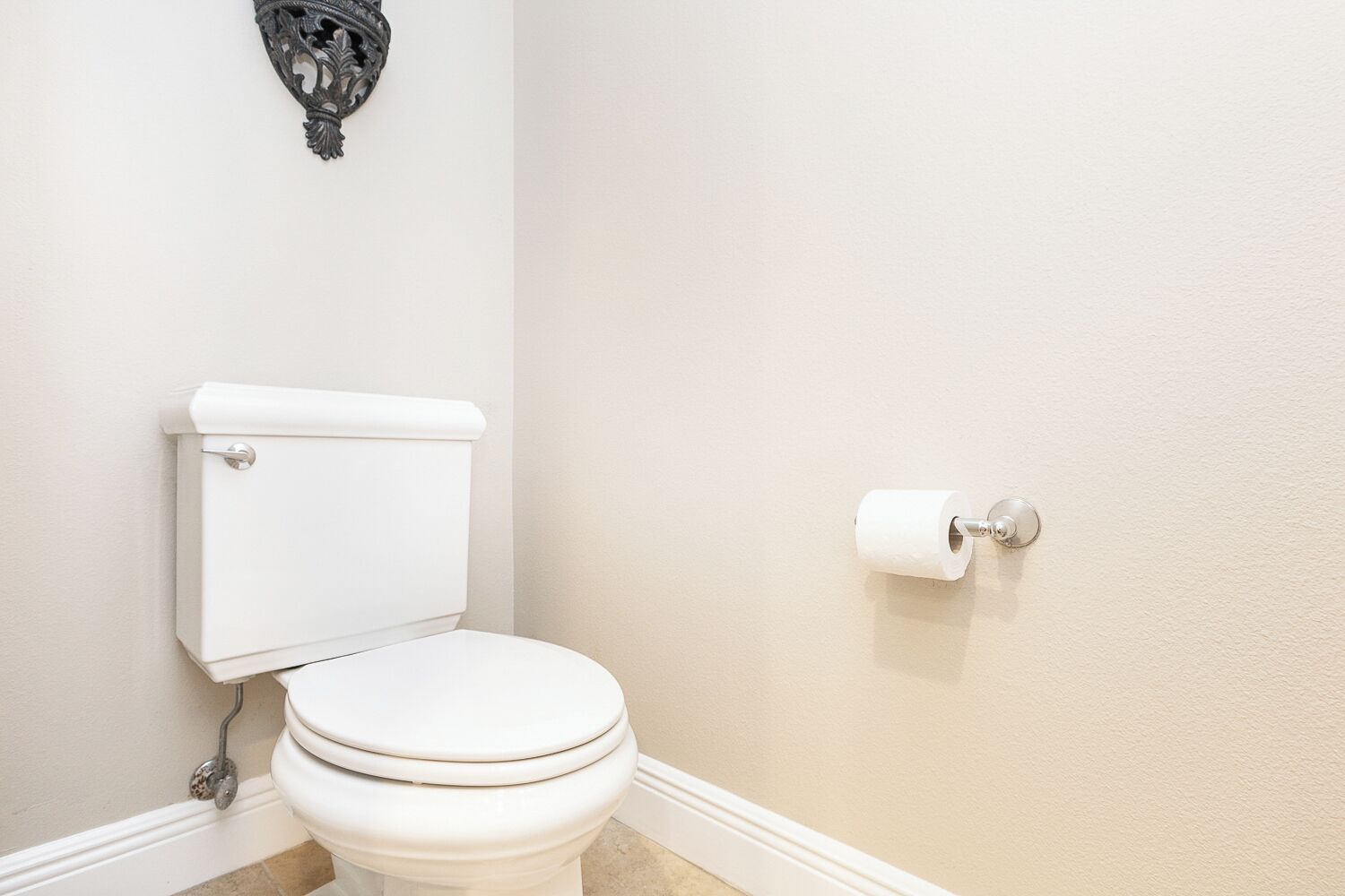 Des toilettes blanches, avec une cuvette et un réservoir, et un porte-rouleau de papier toilette fixé au mur.
