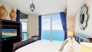 A hotel room with a large bed, a television on a wooden cabinet, a view of the ocean, and a decorative mirror on the wall. - 20th Floor*Stunning Views at Portofino P5-2006 (Pensacola Beach)