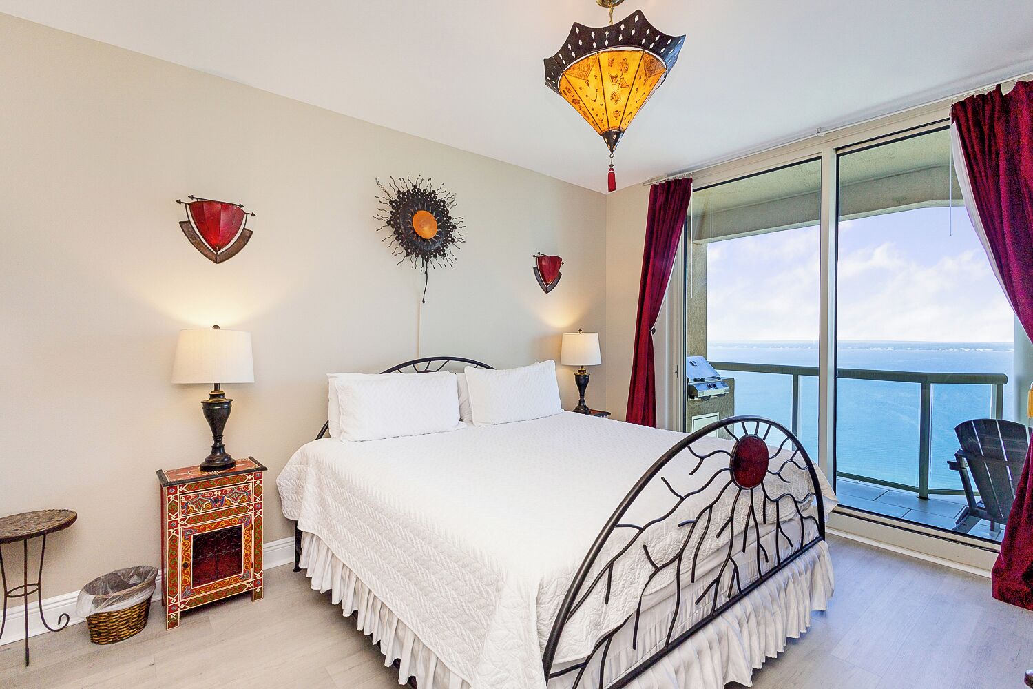 Une chambre d’hôtel comprenant un lit, deux lampes de chevet, un élément décoratif mural, une fenêtre donnant sur la mer et un balcon avec une chaise.