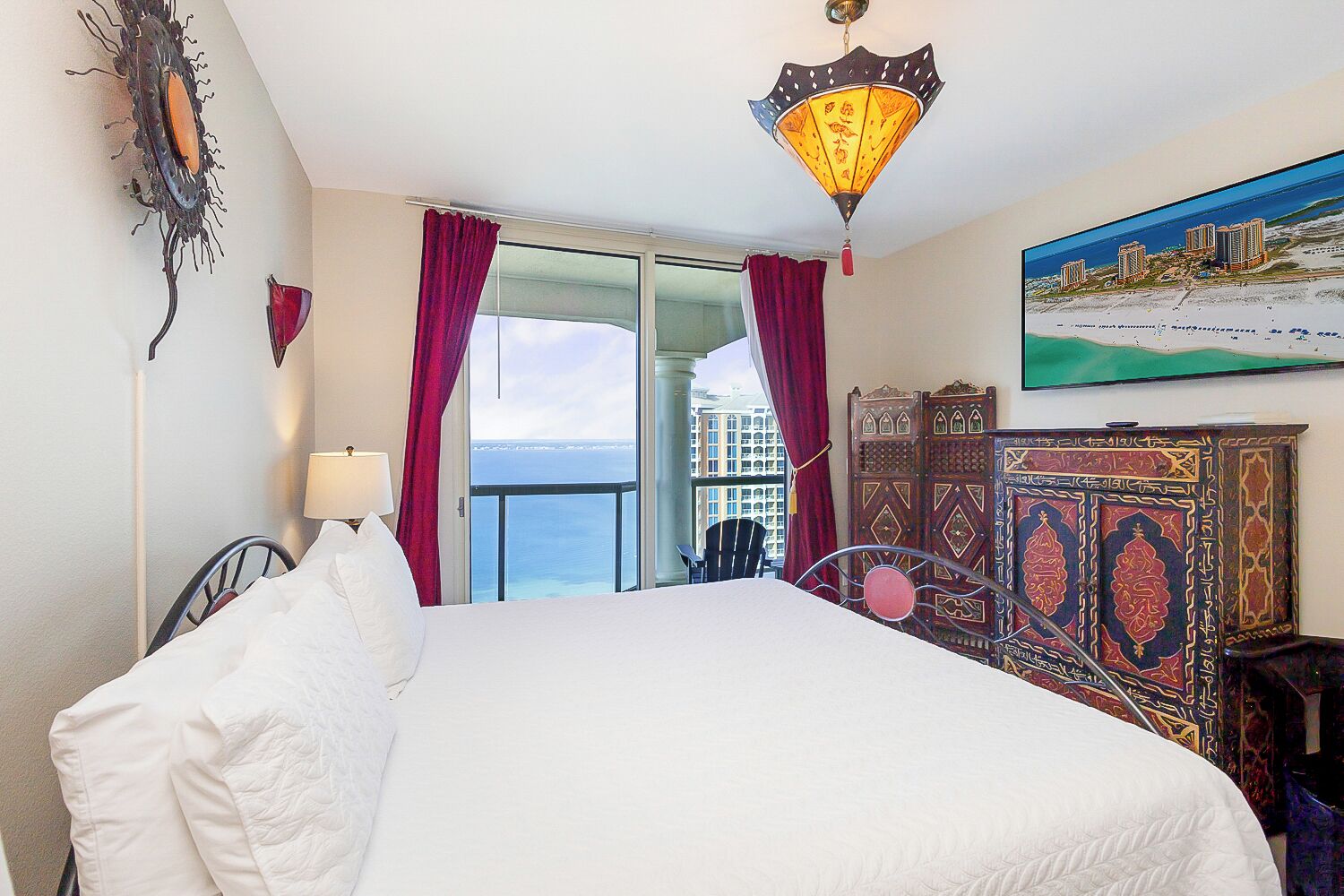 Una habitación de hotel con cama, vista al mar, un cuadro y un aparador decorativo.