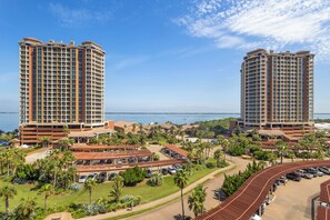 A high-rise hotel with multiple balconies, a parking area, and a view of the sea.