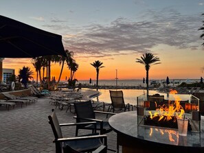 A sunset view from a poolside area with lounge chairs, a fire feature, and palm trees. - P1-1104 - Great 3B at Portofino - Close to Beach! (Pensacola Beach)