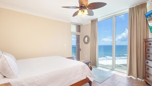 A bedroom with a bed, a ceiling fan, a view of the ocean, and a wooden dresser.