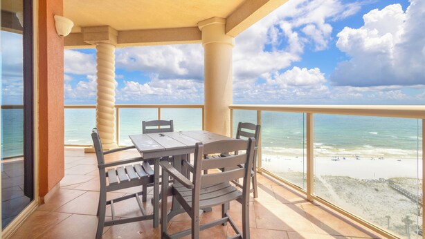 A balcony with a table and chairs, overlooking a beach.
