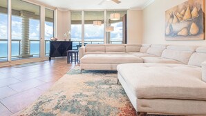 A spacious living room with a large beige sectional sofa, a ceiling fan, and a view of the ocean through large sliding doors.