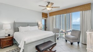 A hotel room with a large bed, a ceiling fan, a view of tall buildings, and a balcony with a chair. - P2-1007 3B Gulf View Condo - Sleeps 10! Great for Families! (Pensacola Beach)