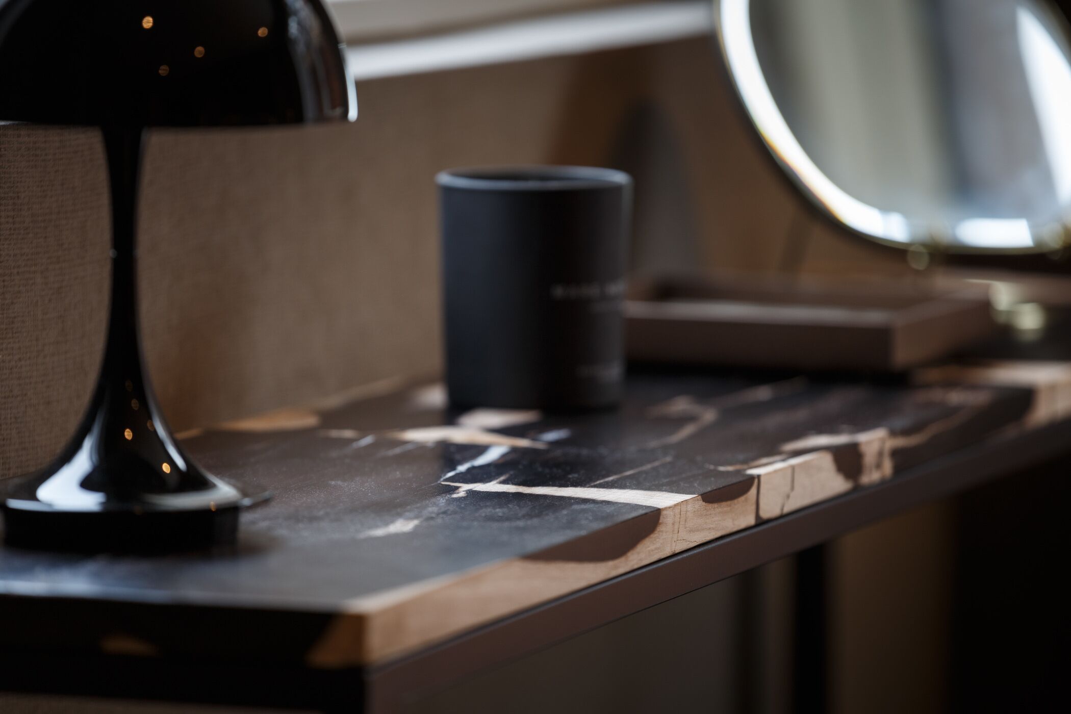Primer plano de un mostrador de madera con una lámpara negra y un objeto cilíndrico negro, posiblemente un recipiente o taza.