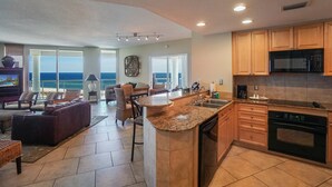 A spacious living area with a large window overlooking the ocean, a kitchen with wooden cabinets and granite countertops, and a cozy seating area with a fireplace. - P3-0807*Gulf View *Tower 3* Closest Beach Access! (Pensacola Beach)