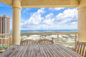 A wooden table and chairs on a balcony with a view of the beach and ocean.