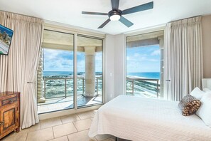 A bedroom with a bed, a ceiling fan, and a large window with a view of the ocean.