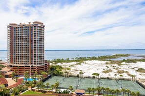 A high-rise hotel with multiple floors, a beach view, and tennis courts.