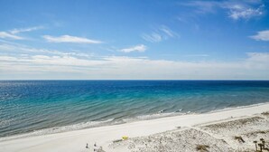 Une plage avec une eau d’un bleu limpide, un rivage sablonneux et quelques constructions.