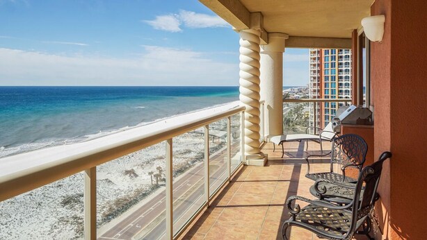 Un balcon avec vue sur la plage et l’océan, comprenant un espace salon extérieur et une balustrade.