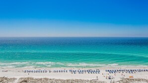 A beach with a clear blue sky and turquoise sea. There are numerous beach umbrellas and people on the sand. - Gulf Front Views*Wraparound Balcony (Pensacola Beach)