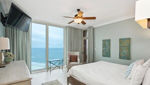 A bedroom with a large bed, a TV, a ceiling fan, a chair, and a view of the ocean. - P3-1901 Stunning 3B Gulf Front - Wrap Around Balcony! (Pensacola Beach)
