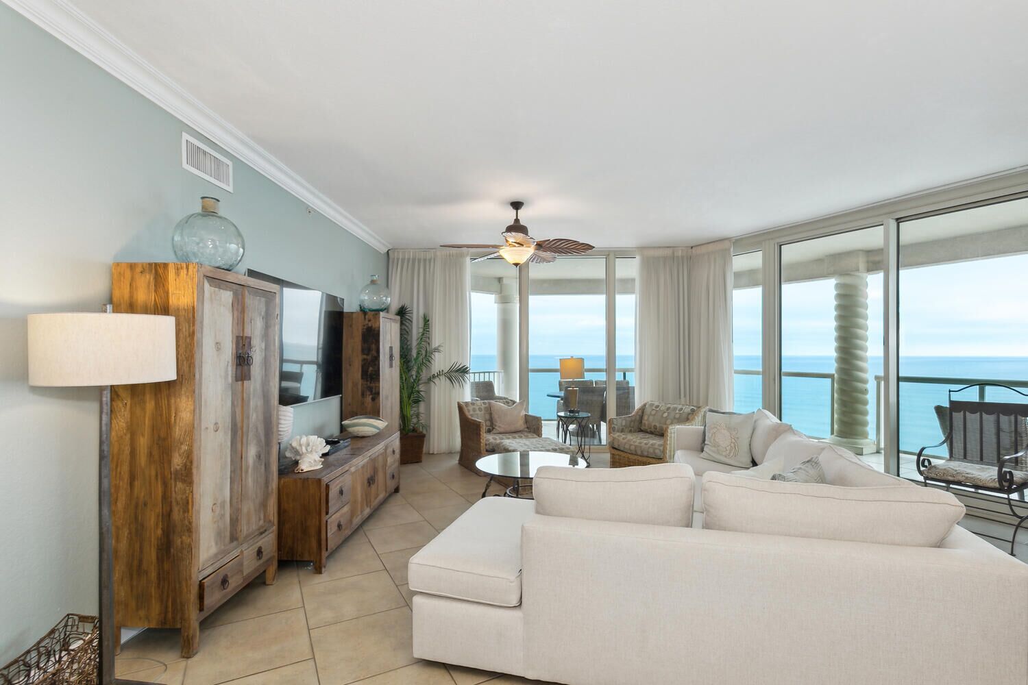 Ein geräumiges Wohnzimmer mit einer großen Couch, einem Holzschrank und einem Fernseher. Es gibt einen Balkon mit Blick aufs Meer.