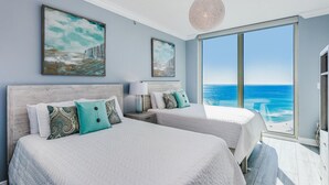 A bedroom with two beds, a large window with a view of the ocean, and artwork on the walls.
