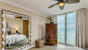 Quarto de hotel com um espelho grande, uma cama, um armário de madeira e vista para o oceano.