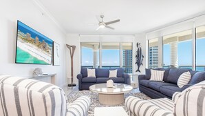 A spacious living room with a large window, a ceiling fan, and a view of the ocean. - P4-1304 Pristine 3B Gulf View in Tower 4! (Pensacola Beach)