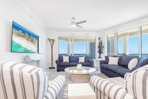 A spacious living room with a large window, a ceiling fan, and a view of the ocean. - P4-1304 Pristine 3B Gulf View in Tower 4! (Pensacola Beach)