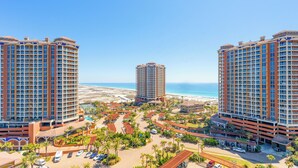 A resort with multiple high-rise buildings, a beach, and a parking area with palm trees. - P4-1304 Pristine 3B Gulf View in Tower 4! (Pensacola Beach)