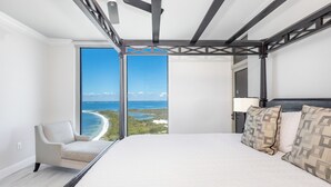 A bedroom with a large bed, a view of the ocean, a ceiling fan, and a chair by the window. - P4-1304 Pristine 3B Gulf View in Tower 4! (Pensacola Beach)