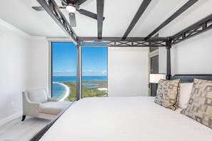 A bedroom with a large bed, a view of the ocean, a ceiling fan, and a chair by the window. - P4-1304 Pristine 3B Gulf View in Tower 4! (Pensacola Beach)