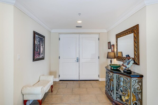 Un pasillo con una puerta blanca, un banco, una consola decorativa con una lámpara y un espejo.