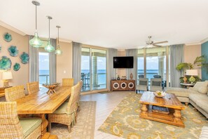 Un salón amplio con una mesa de comedor de madera, sillas de mimbre, una mesa baja y un televisor de pantalla plana grande.