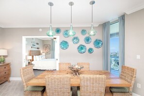 A dining area with a wooden table and wicker chairs, a glass bowl centerpiece, and decorative wall art.