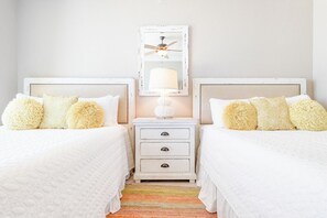A bedroom with two beds, a nightstand, a lamp, and a ceiling fan.