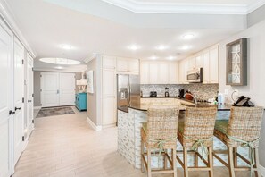 A modern kitchen with white cabinetry, a central island with bar seating, and a built-in microwave.