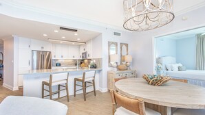 A modern kitchen with white cabinets, a stainless steel refrigerator, and a wooden dining table with chairs.