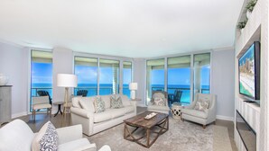A spacious living room with a large window overlooking the ocean, a flat-screen TV mounted on the wall, and a cozy seating area with a coffee table.