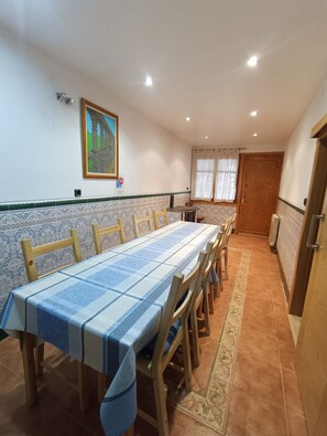 A dining area with a long table, chairs, a painting on the wall, and a door.