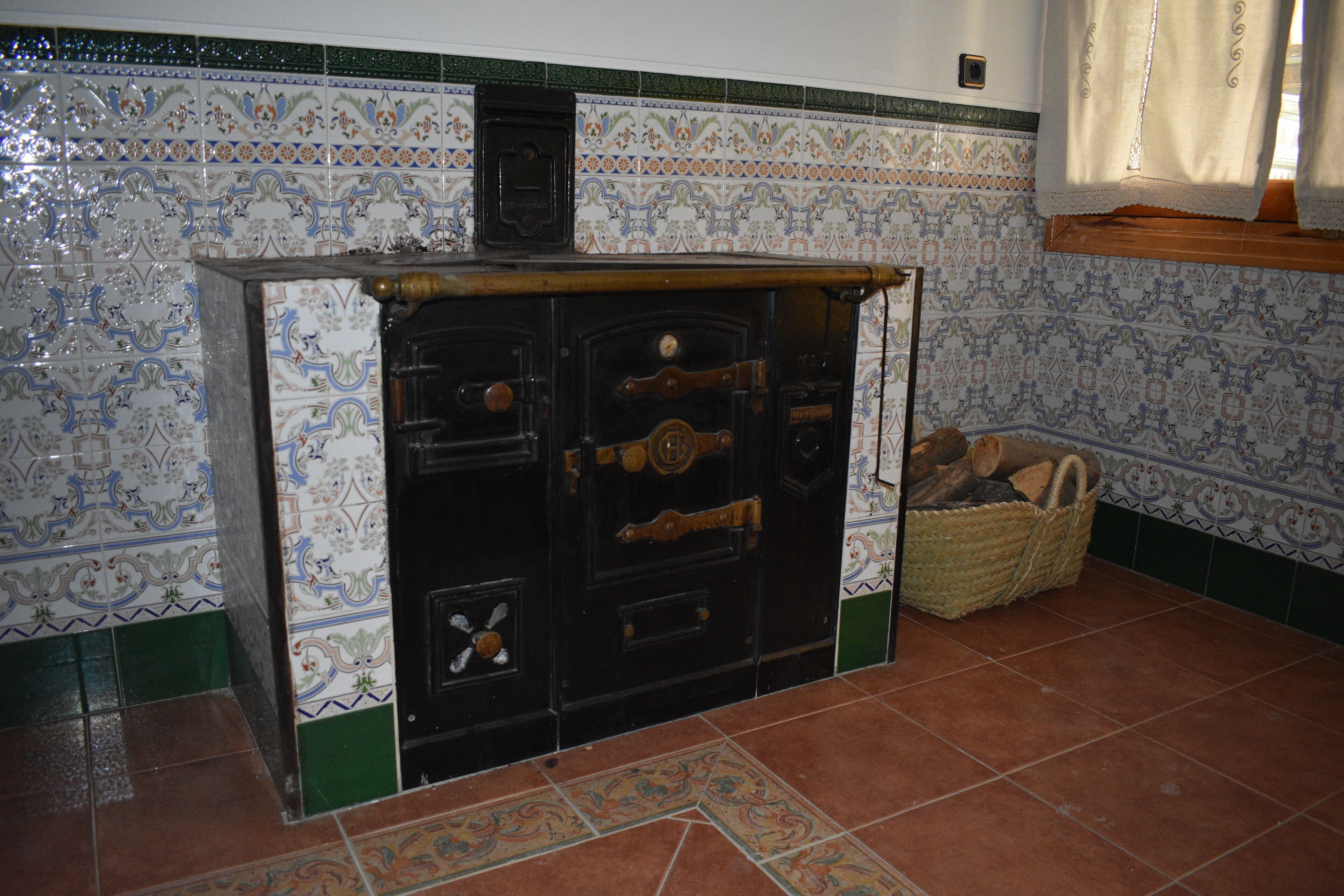 A kitchen with a tiled backsplash, a stove, and a basket of firewood.